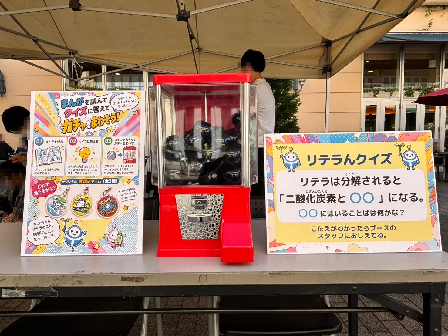 「まんがを読んでクイズに答えてガチャをまわそう!」の掲示と赤いガチャガチャとリテラんクイズの掲示